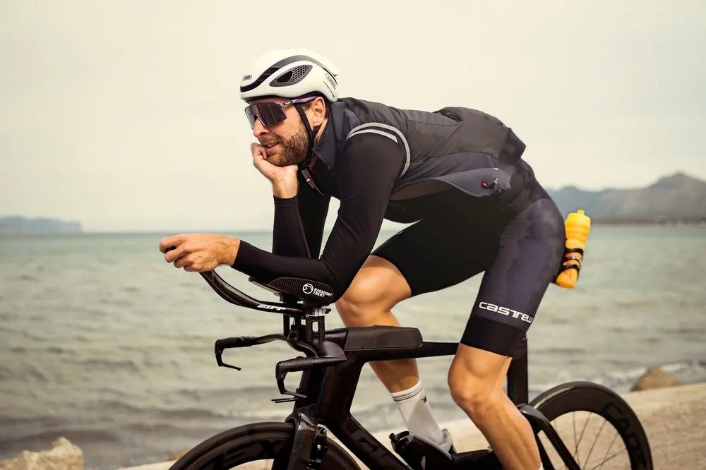 Nick lacht auf dem Zeitfahrrad an der Küste von Mallorca, dahinter Meer und Berge