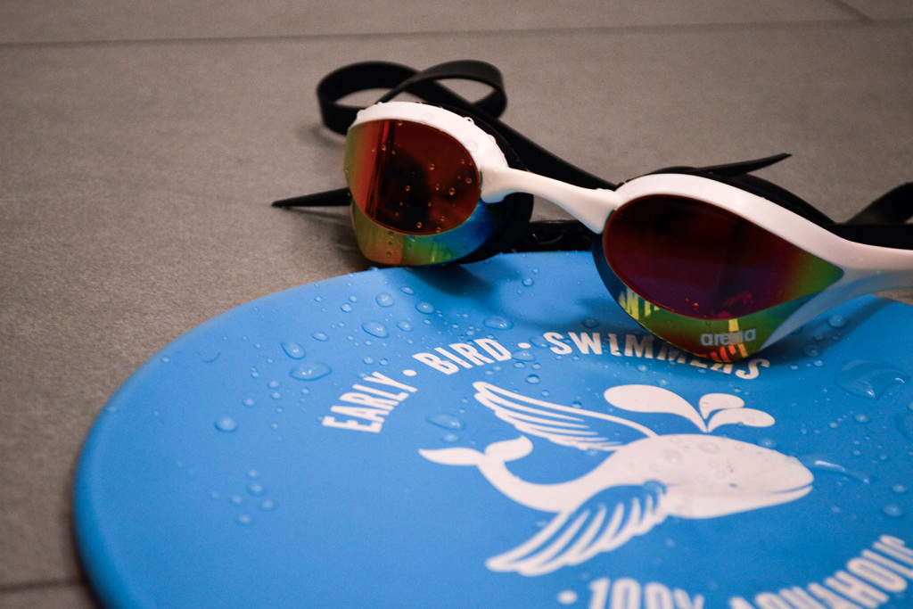 Verspiegelte Schwimmbrille von Arena liegt auf einer nassen blauen Badekappe der Early Bird Swimmers