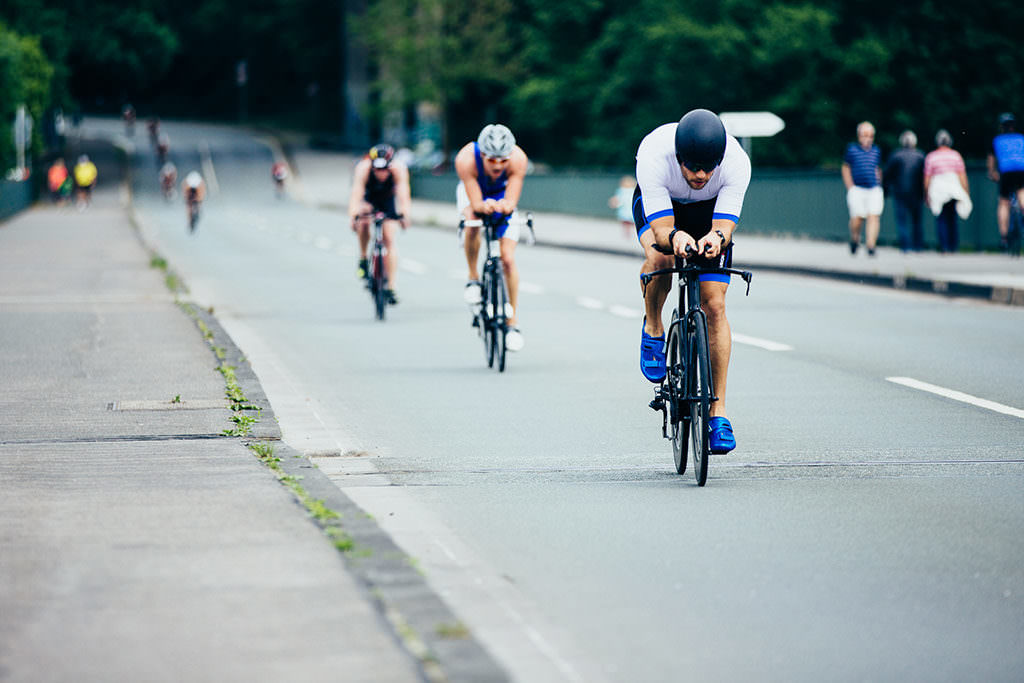 Triathlet in Aeroposition auf der Radstrecke des Triathlons in Hagen, dahinter weitere Radfahrer und Zuschauer