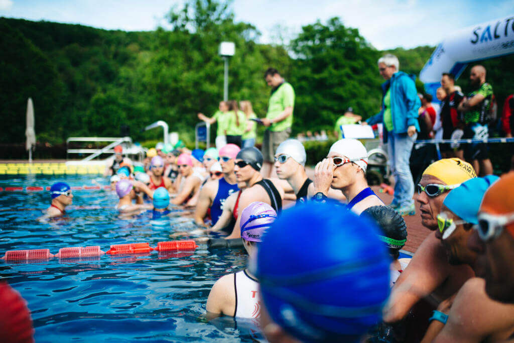 Triathleten mit bunten Badekappen und Schwimmbrillen warten im Freibad auf den Schwimmstart beim Triathlon Hagen