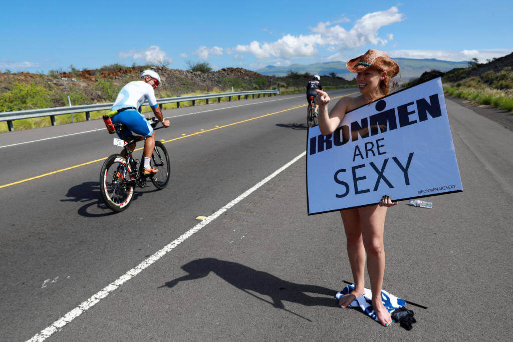 Zuschauerin mit Cowboyhut hält ein Schild mit der Aufschrift Ironmen are sexy an der Radstrecke des Ironman Hawaii