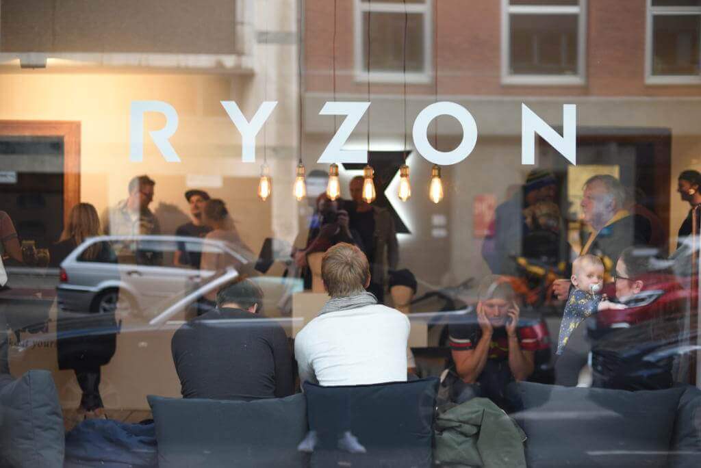 Blick durch die Schaufensterscheibe mit Ryzon-Schriftzug auf Gäste bei der Eröffnung des Showrooms in Köln