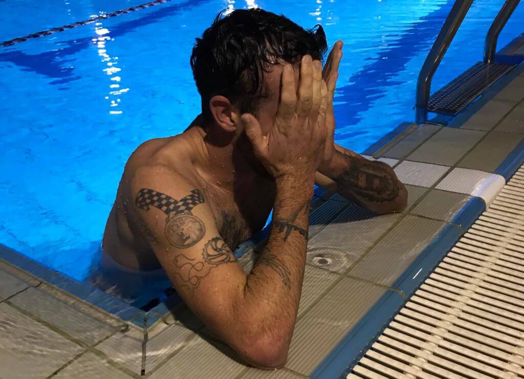Niclas Bock stützt sich nach dem Schwimmtraining am Beckenrand ab und hält sich die Hand vors Gesicht