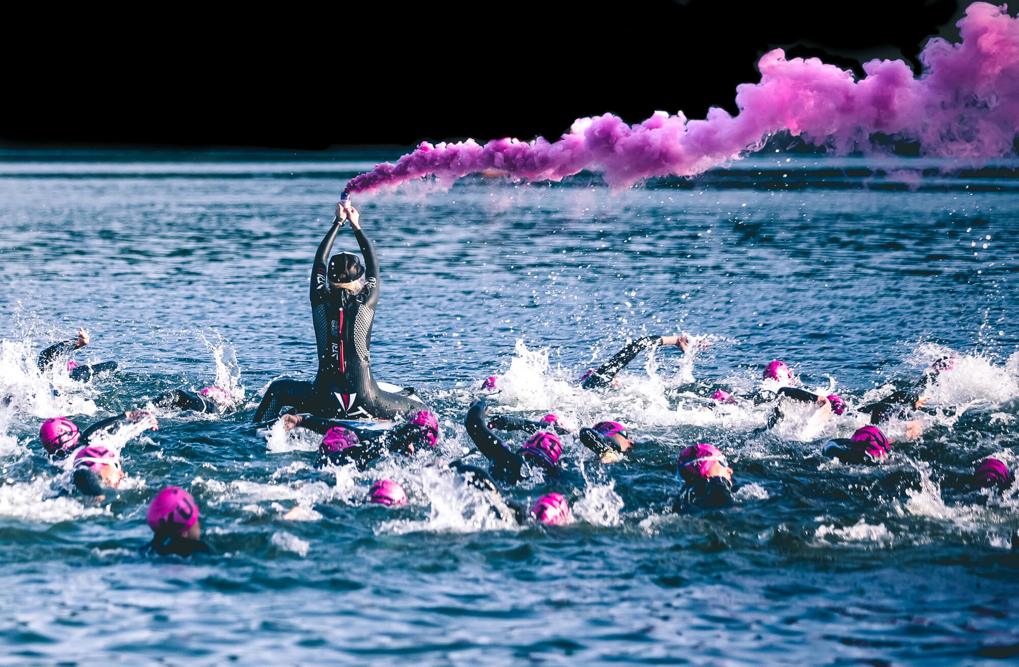 Inszenierter Schwimmstart beim Allgäu Triathlon mit pinker Rauchfackel und Schwimmern mit pinken Badekappen im See