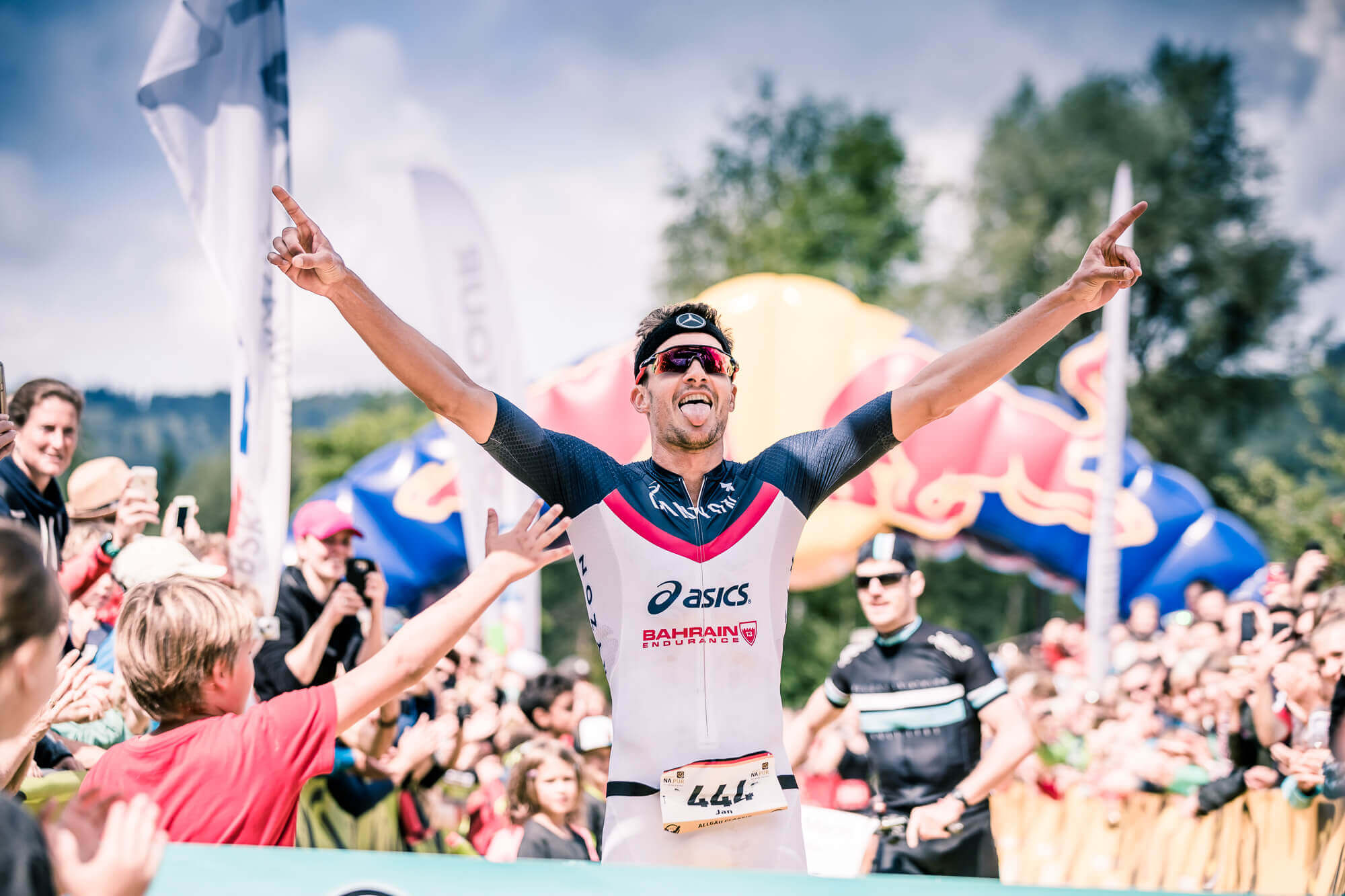 Jan Frodeno jubelt mit ausgebreiteten Armen im Ziel des Allgäu Triathlon, Kinder klatschen ihn ab