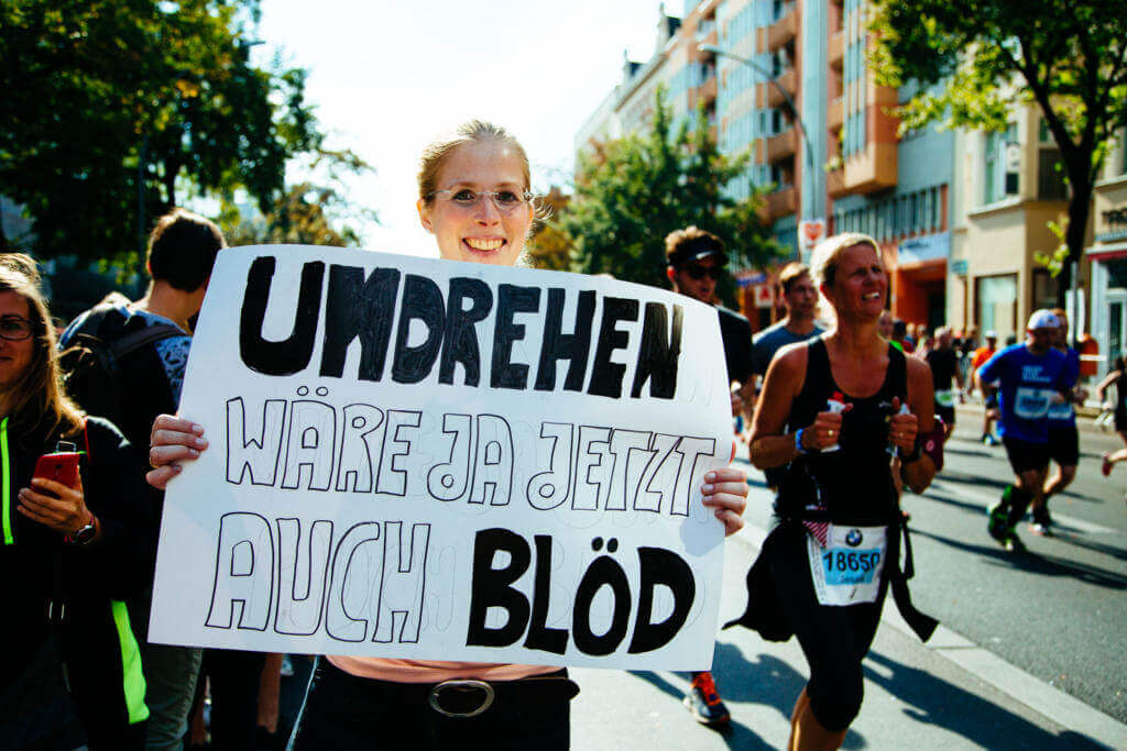 Lachende Zuschauerin hält beim Berlin-Marathon 2016 ein Schild mit der Aufschrift Umdrehen wäre ja jetzt auch blöd