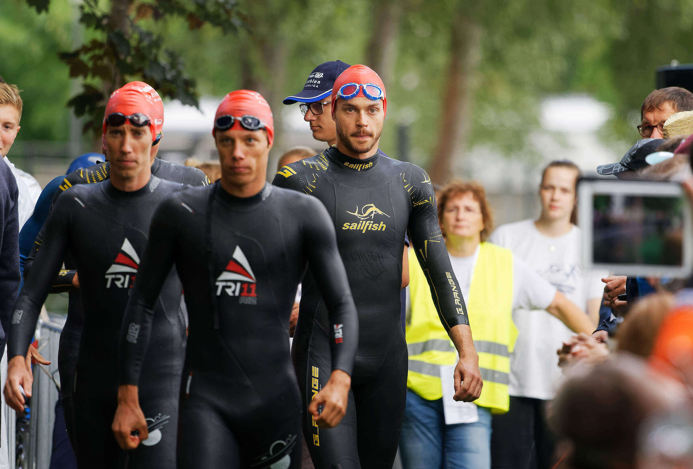Franz Löschke und Jonathan Zipf mit weiteren Triathleten in Neoprenanzügen und Badekappen auf dem Weg zum Schwimmstart