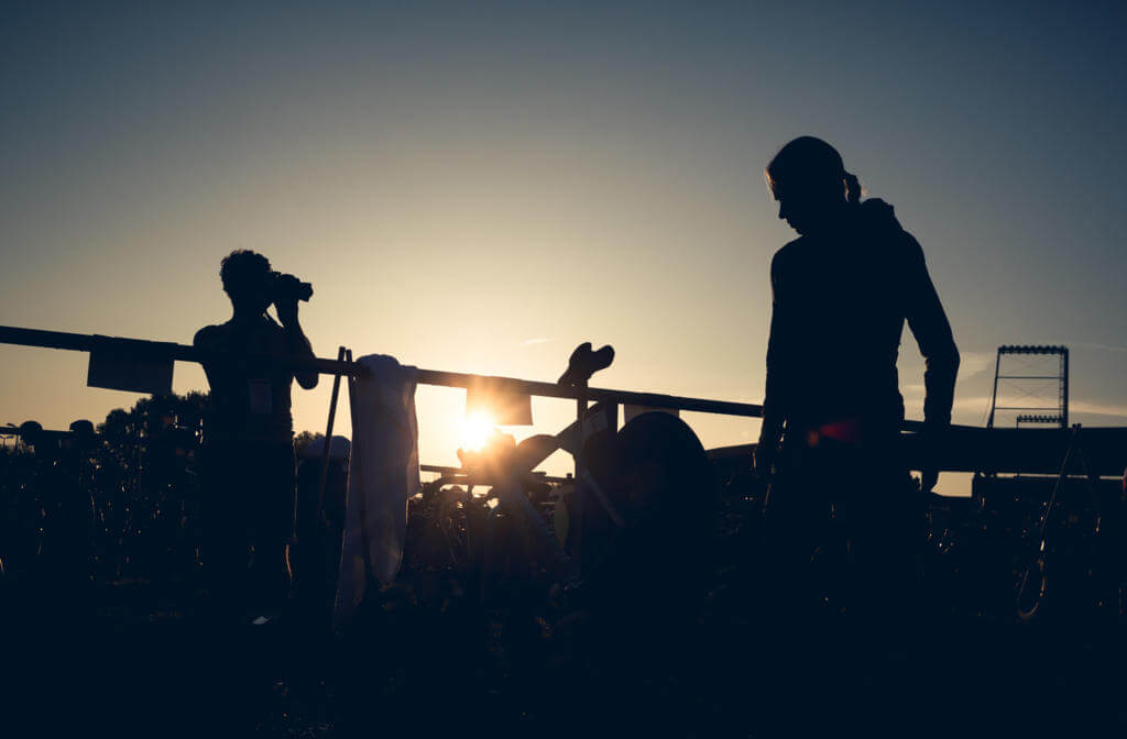 Silhouetten zweier Personen zwischen Rädern in der Wechselzone des Ironman 70.3 St. Pölten im Gegenlicht, eine fotografiert