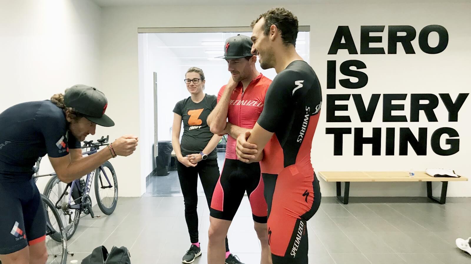 Golo Röhrken, Tim Don und weitere Personen vor dem Wandschriftzug Aero is everything beim Windtunnel-Test von Specialized