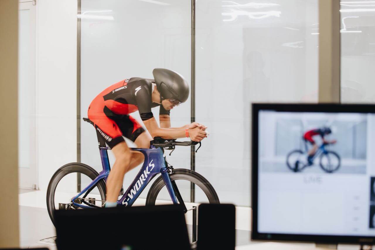 Golo Röhrken in Aeroposition auf einem S-Works-Zeitfahrrad bei der Messung im Specialized-Windtunnel, daneben ein Monitor