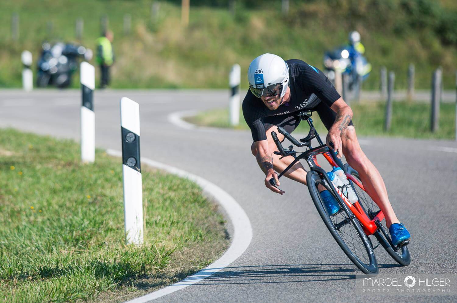 Niclas Bock legt sich beim Allgäu Triathlon mit dem Zeitfahrrad in eine Kurve, dahinter Begleitmotorräder