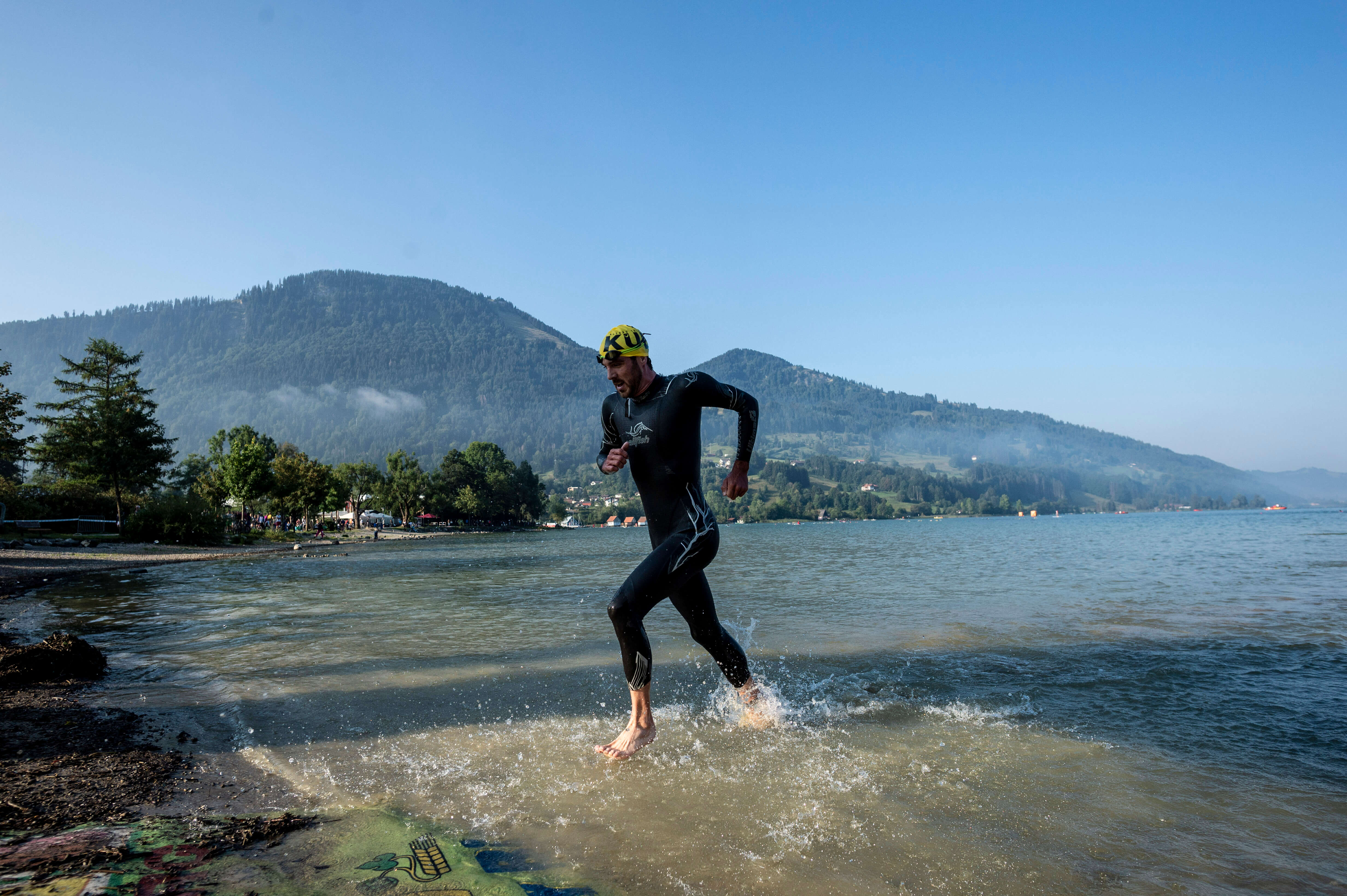 Niclas Bock läuft im Neoprenanzug aus dem Großen Alpsee, Schwimmausstieg beim Allgäu Triathlon vor Bergkulisse