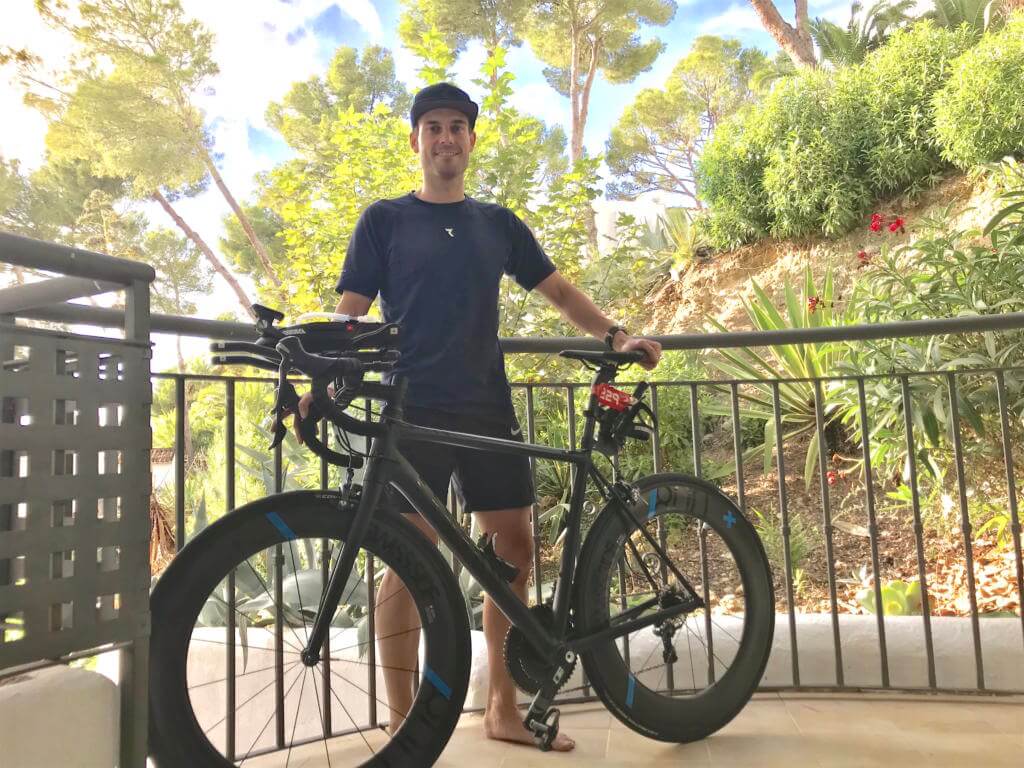 Daniel Marx steht vor seinem Saisonfinale auf Mallorca mit seinem Zeitfahrrad auf einer Terrasse, dahinter Pinien
