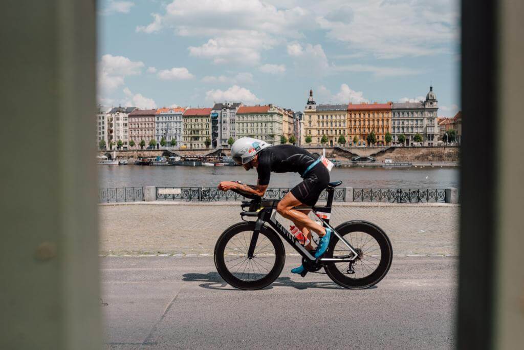 Triathlet auf dem Zeitfahrrad an der Moldau bei der Challenge Prag, im Hintergrund bunte Altbauten