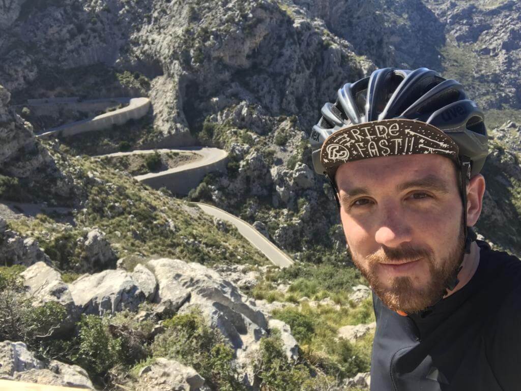 Niclas Bock mit Radhelm und Ride-Fast-Kappe beim Selfie vor Serpentinen in einer felsigen Berglandschaft