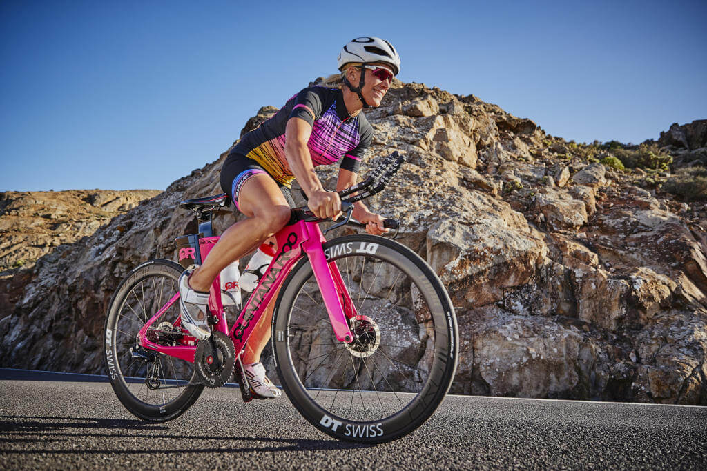 Anja Ippach fährt auf einem pinken Zeitfahrrad mit DT-Swiss-Laufrädern vor Felsen unter blauem Himmel