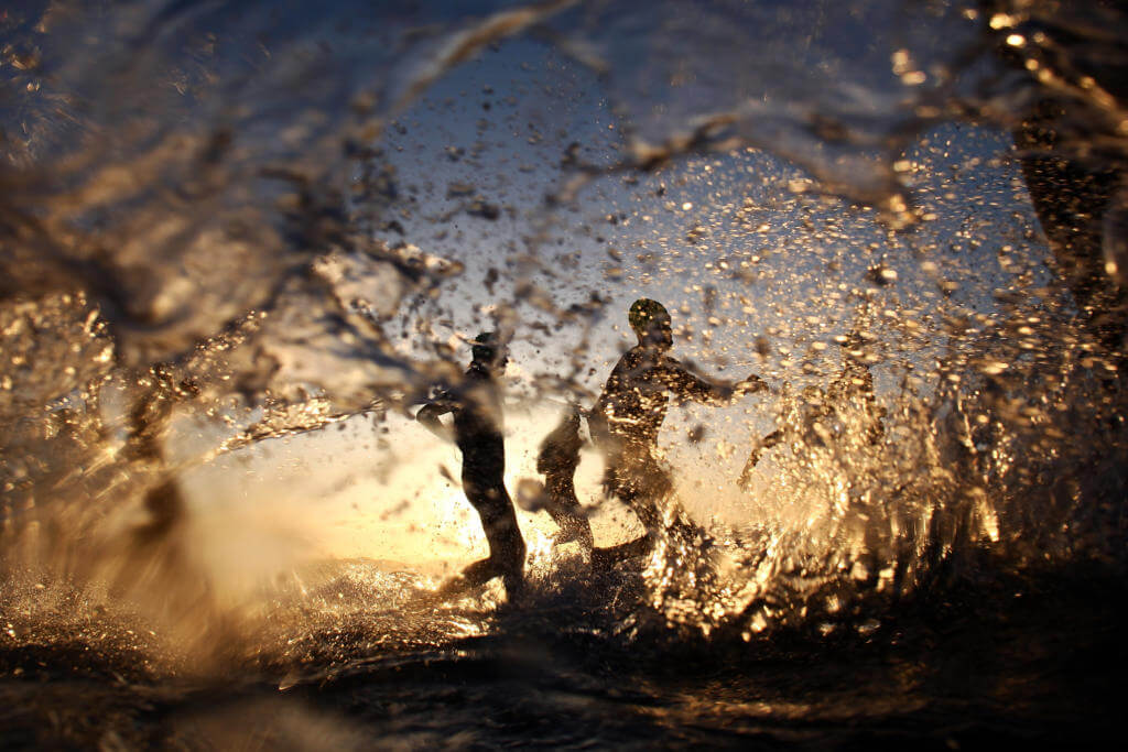 Silhouetten von Athleten laufen im Gegenlicht durch aufspritzendes Wasser, Schwimmstart beim Ironman 70.3 Marbella