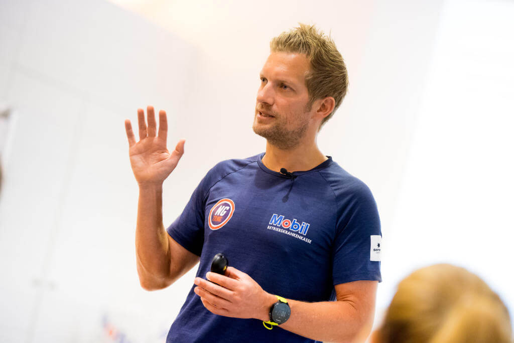 Triathlon-Coach Nils Goerke spricht mit erhobener Hand zu Teilnehmern im Trainingslager