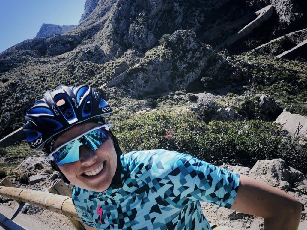 Tamara Hitz mit Radhelm und verspiegelter Sonnenbrille lacht beim Selfie vor felsigen Bergen