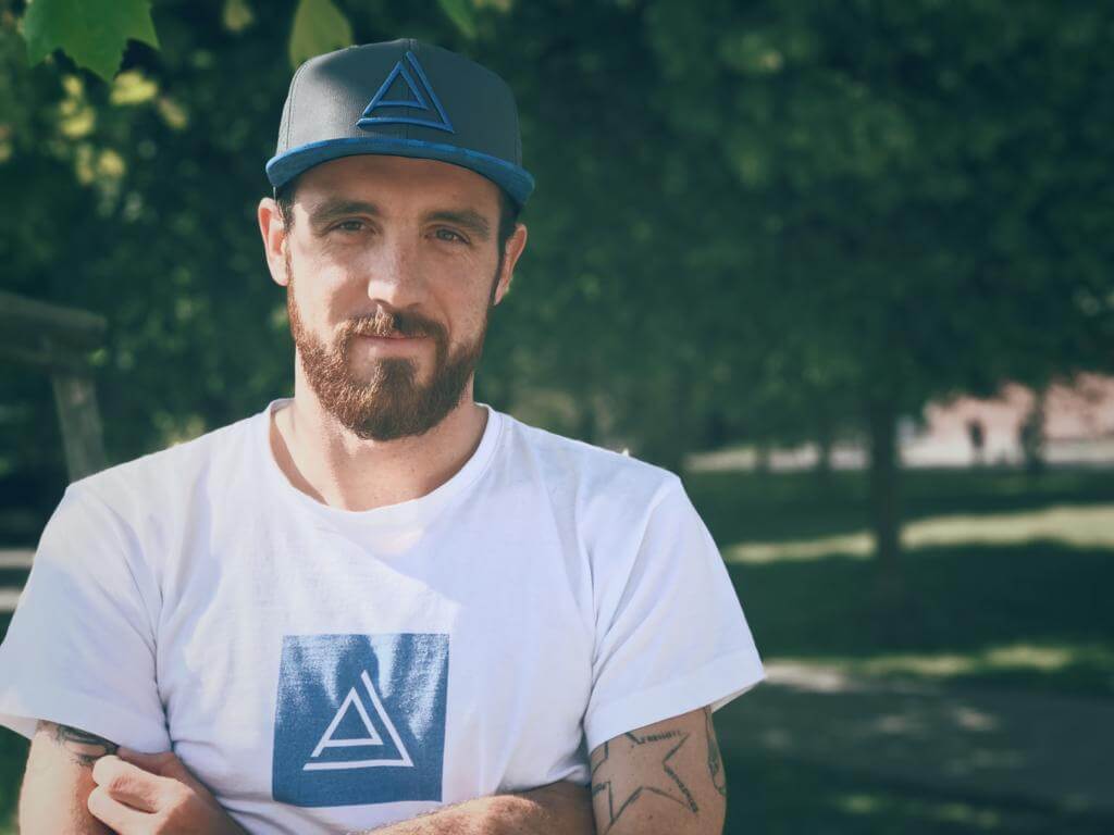 Niclas Bock mit Basecap und weißem T-Shirt steht mit verschränkten Armen im Grünen