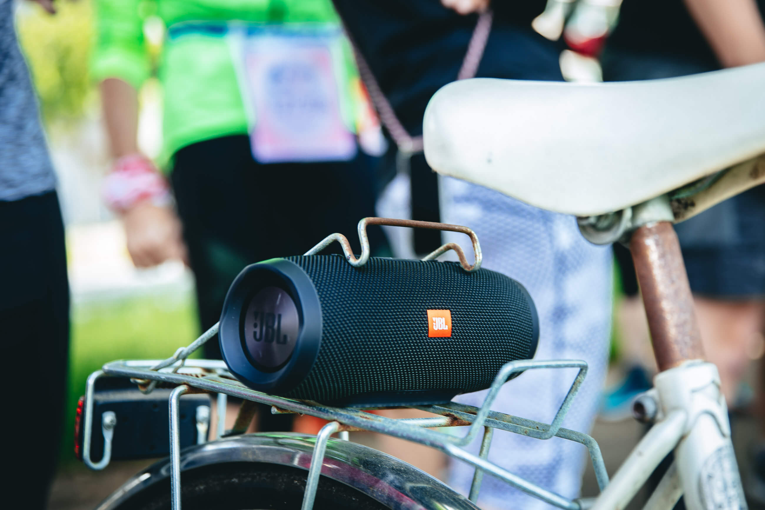 Bluetooth-Box auf dem Gepäckträger eines Fahrrads, dahinter unscharf Läufer beim Wings for Life App Run Düsseldorf