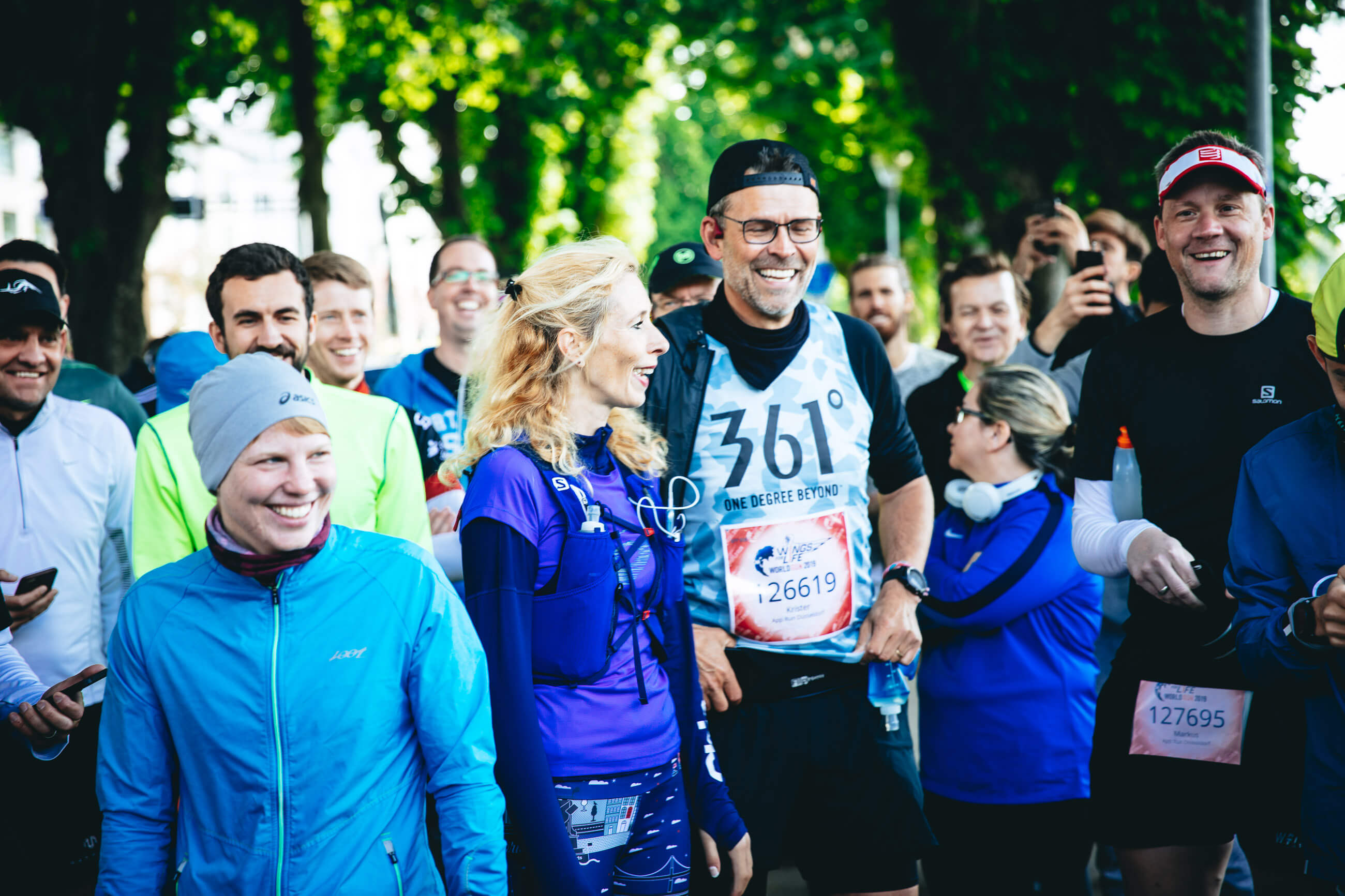 Lachende Teilnehmer mit Startnummern in der Menge vor dem Start des Wings for Life App Run Düsseldorf