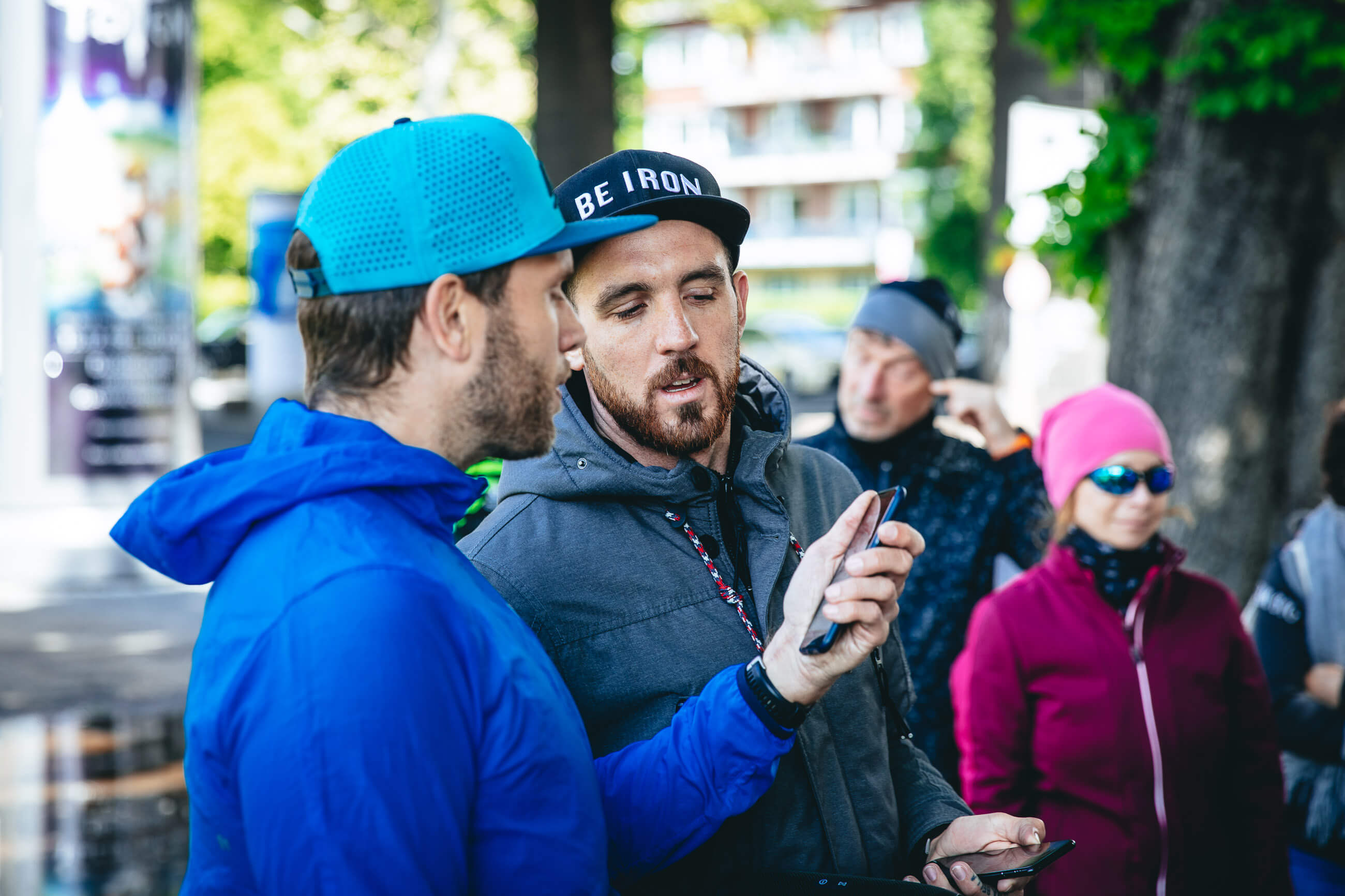 Zwei Männer mit Kappen schauen gemeinsam auf ein Smartphone, dahinter Teilnehmer des Wings for Life App Run Düsseldorf
