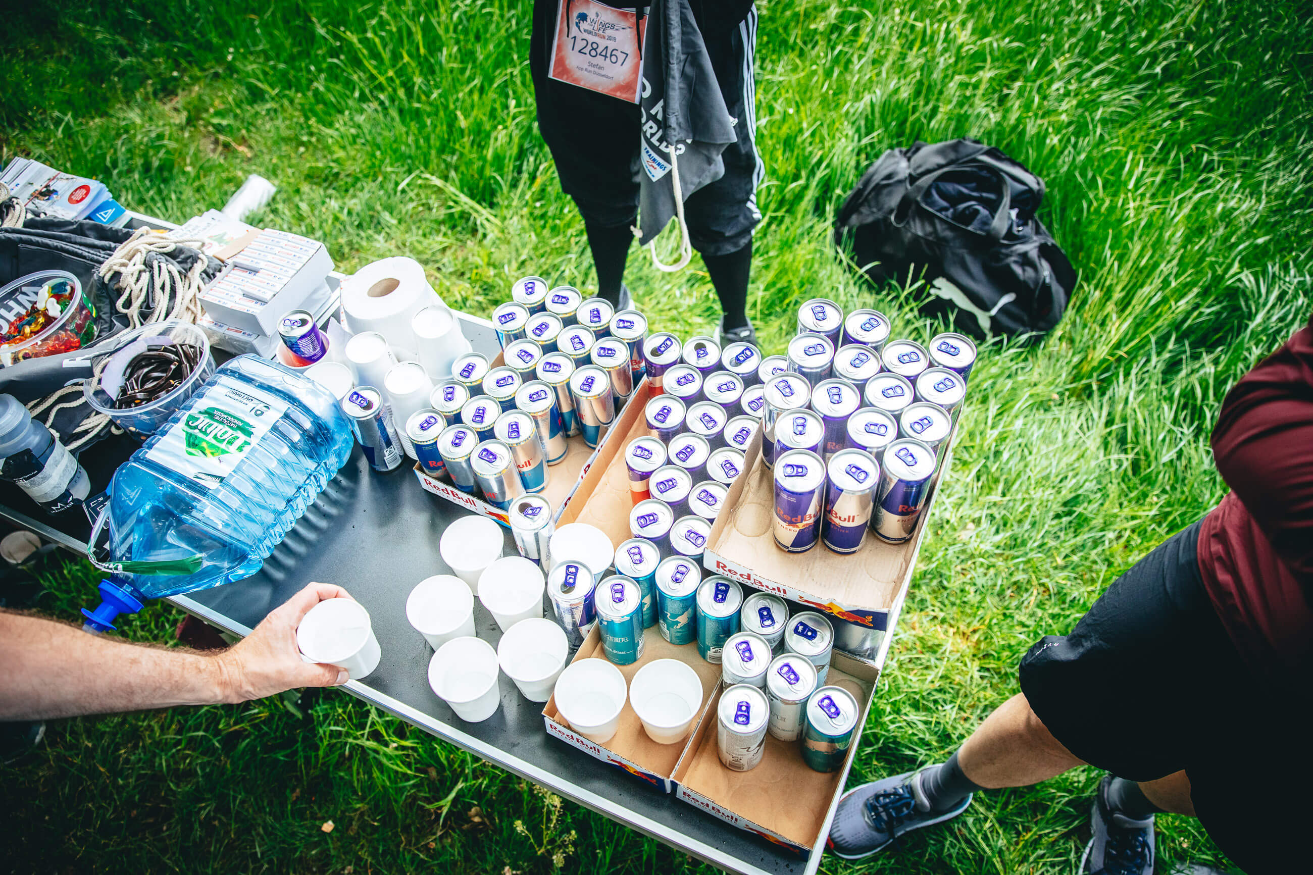 Verpflegungstisch auf der Wiese mit Bechern, Wasserkanister und vielen Red-Bull-Dosen, Wings for Life App Run Düsseldorf