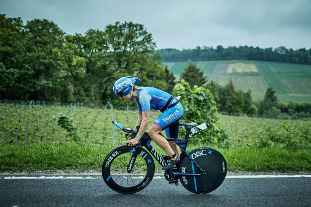 Triathletin Daniela Bleymehl in Aeroposition auf dem Zeitfahrrad mit Scheibenrad, im Hintergrund Weinberge