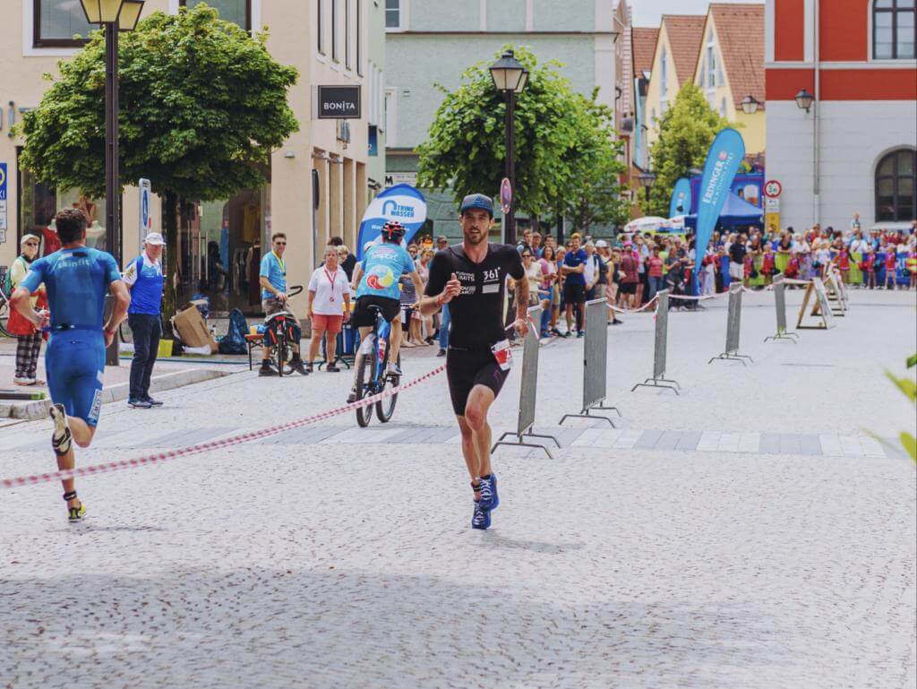 Niclas Bock läuft im schwarzen Einteiler über das Kopfsteinpflaster beim Stadttriathlon Erding, Zuschauer am Rand