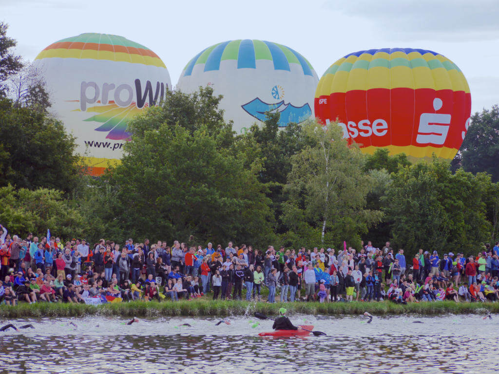 Heißluftballons hinter dicht gedrängten Zuschauern am Kanalufer beim Schwimmstart der Challenge Roth 2016