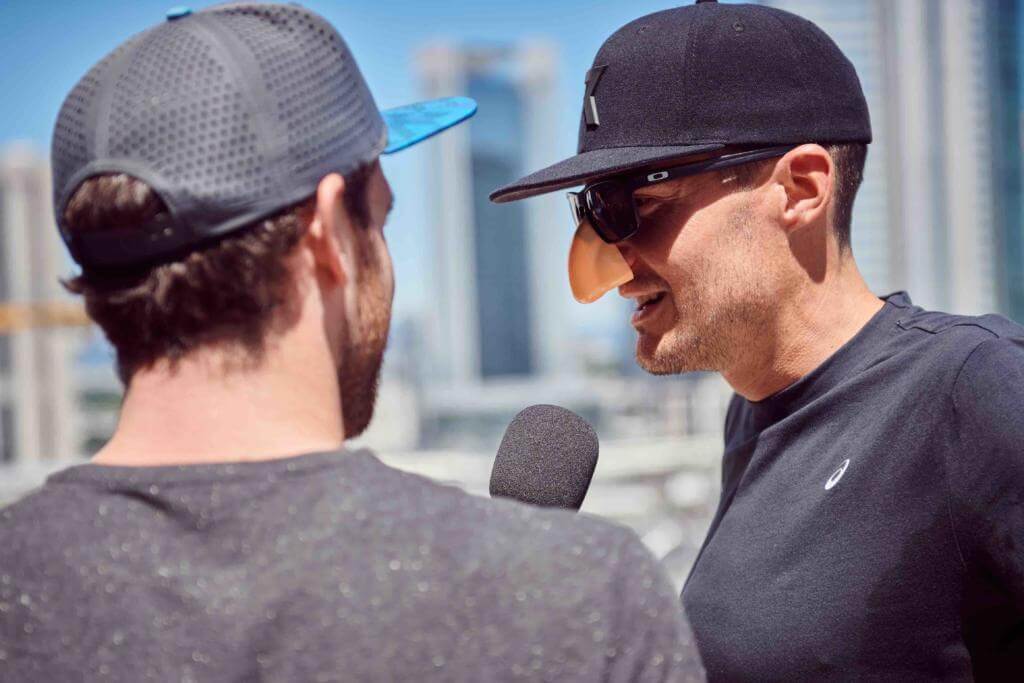 Jan Frodeno mit Kappe, Sonnenbrille und Spaßnase im Interview vor der Frankfurter Skyline