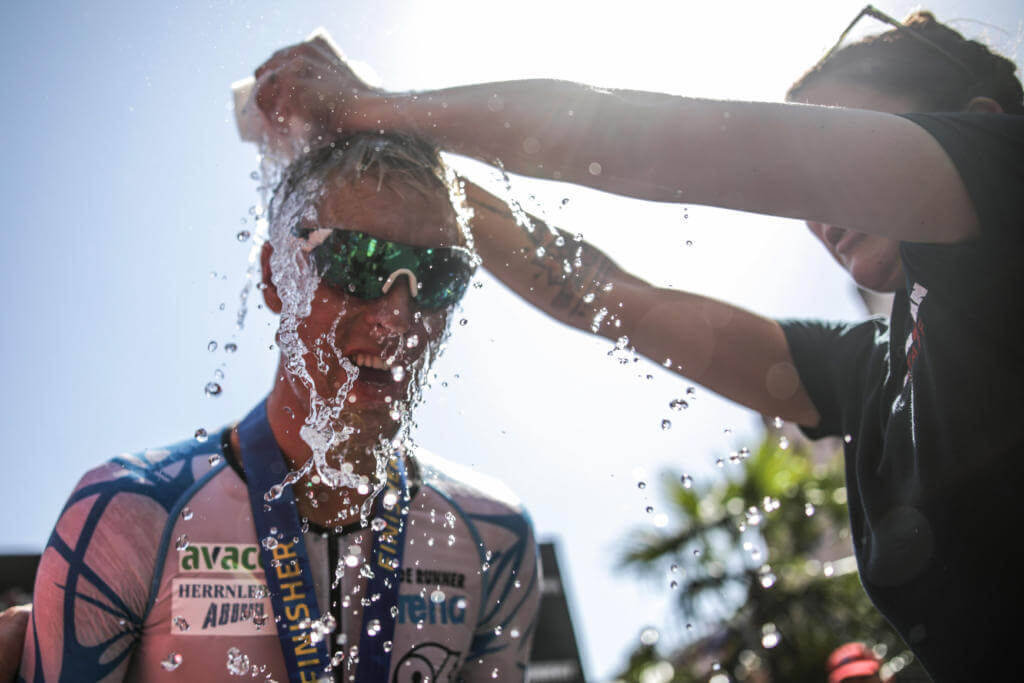 Wasser wird einem Finisher mit Medaille beim Ironman Frankfurt zur Abkühlung über den Kopf gegossen