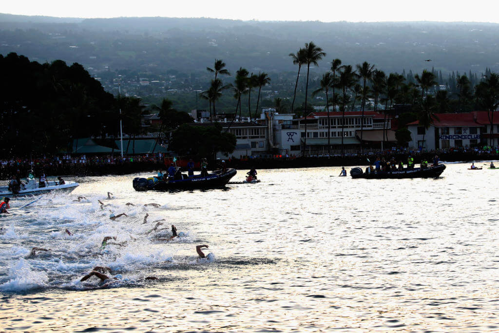 Schwimmer beim Start des Ironman Hawaii 2017 in der Bucht von Kailua-Kona, dahinter Palmen und Zuschauer