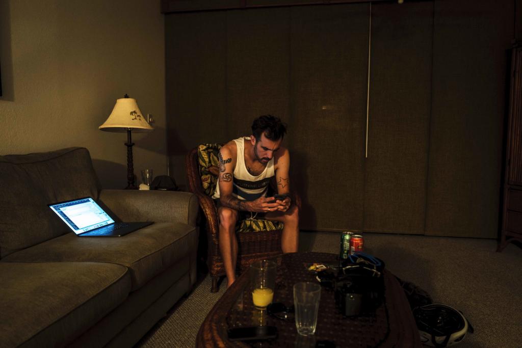Niclas Bock sitzt abends im abgedunkelten Wohnzimmer auf Hawaii und schaut auf sein Smartphone