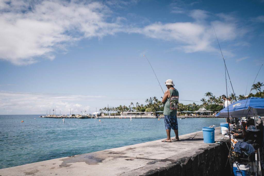Angler an der Ufermauer am Ali'i Drive in Kailua-Kona, im Hintergrund Pier und Palmen