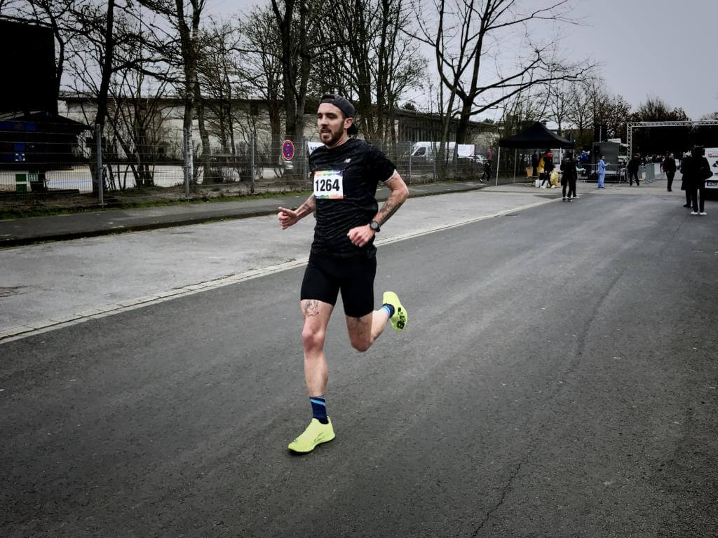 Niclas Bock läuft mit Startnummer 1264 und neongelben Schuhen bei einem Straßenlauf