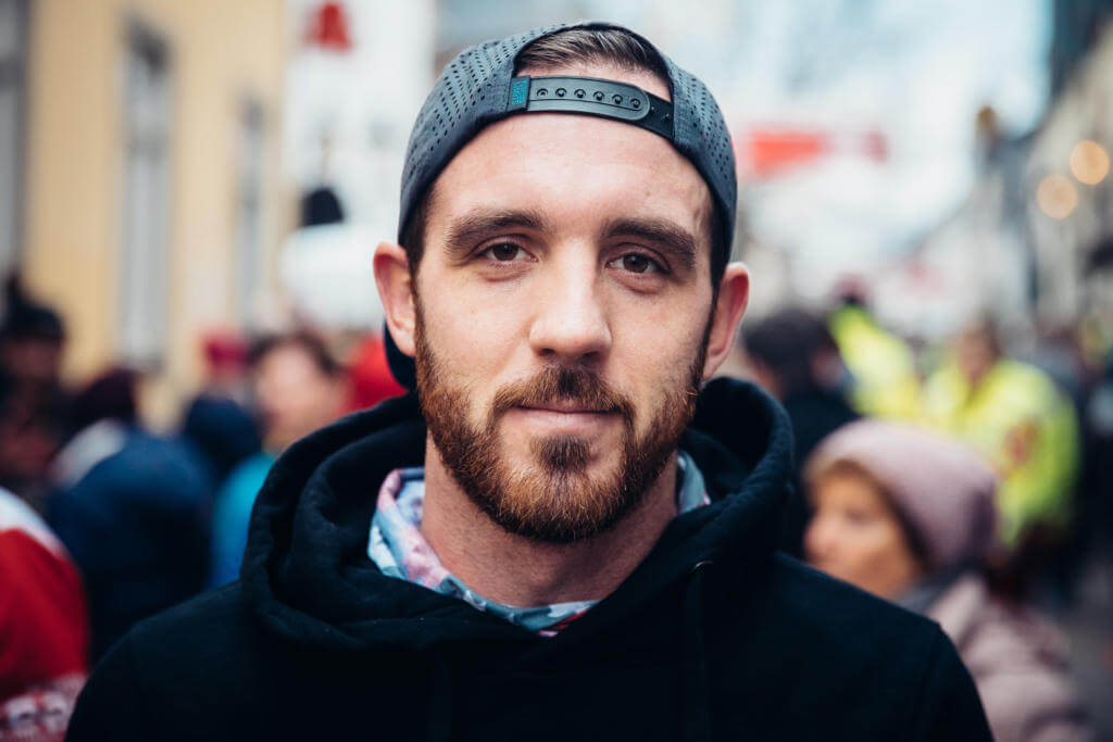 Niclas Bock mit rückwärts getragener Kappe und schwarzem Hoodie blickt in einer belebten Straße in die Kamera