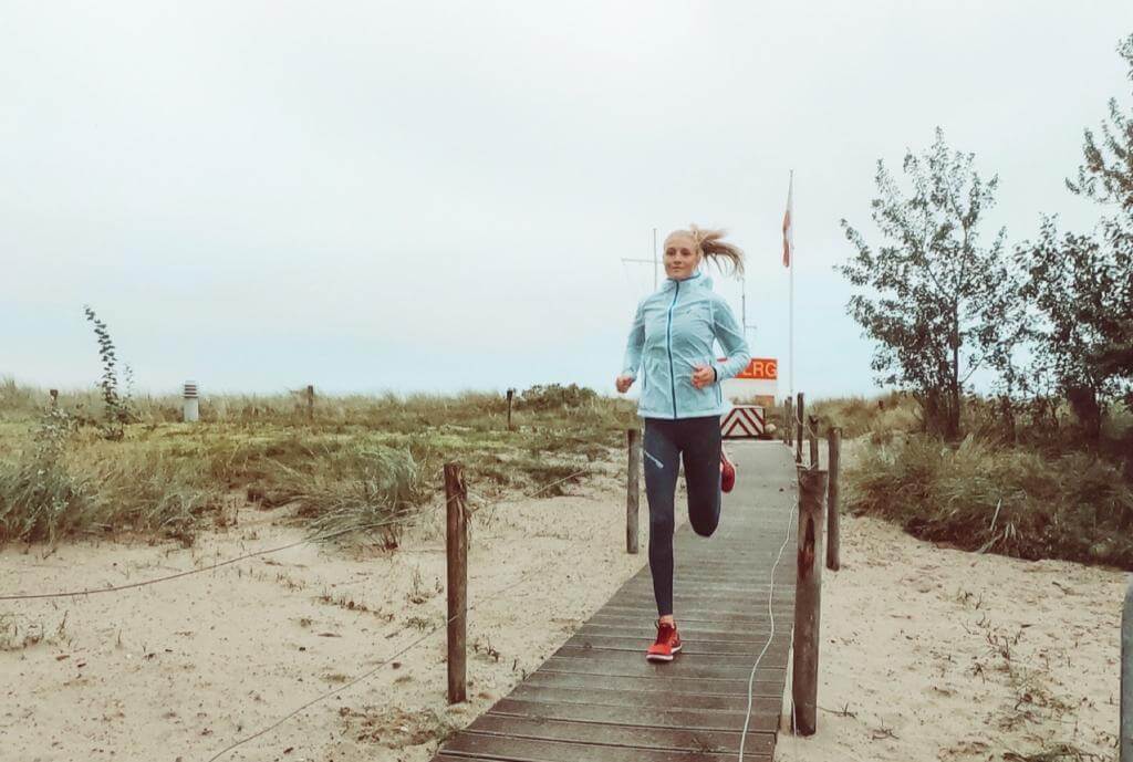 Imke Oelerich läuft in hellblauer Jacke über einen Holzsteg durch die Dünen