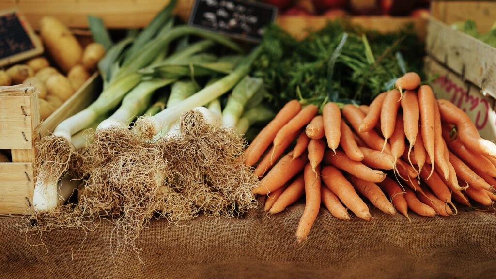 Frischer Lauch, Möhren mit Grün und Kartoffeln in Holzkisten an einem Marktstand