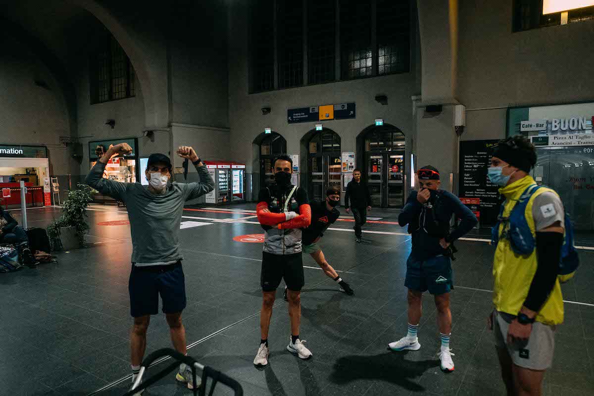 Läufergruppe mit Masken und Laufwesten vor dem Start des Ultralaufs in einer Bahnhofshalle