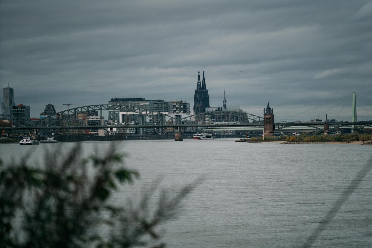 Blick über den Rhein auf die Kölner Skyline mit Dom und Brücken unter grauem Himmel
