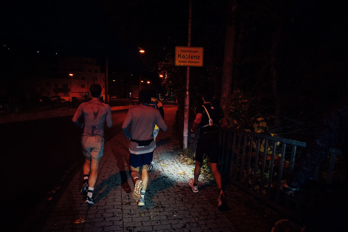 Läufer mit Stirnlampen laufen nachts an einem Ortsschild von Koblenz vorbei, Start des Ultralaufs