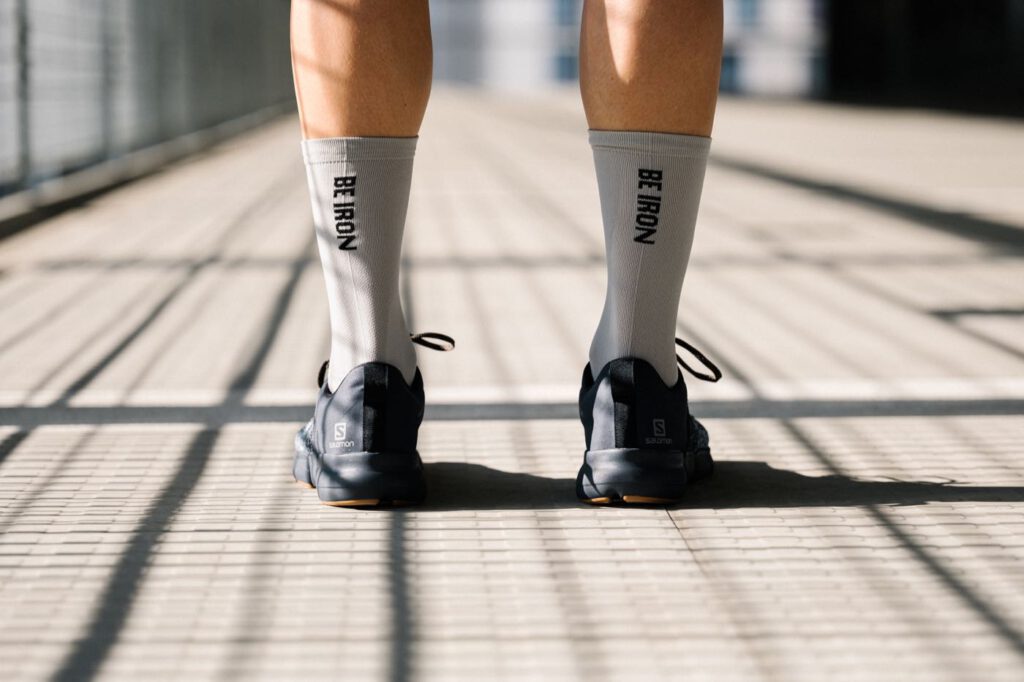 Graue BE IRON Performance Socks von Fe226 mit schwarzem Schriftzug in schwarzen Laufschuhen