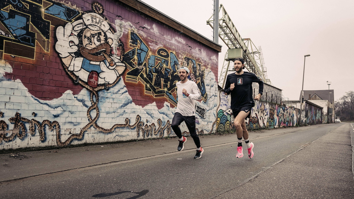 Bocki und Nick joggen durch ein Industriegebiet vor Mauern mit Graffiti