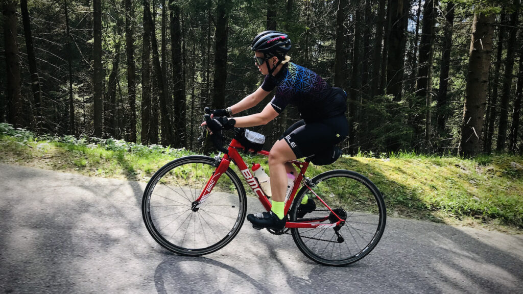 Eine Radfahrerin fährt durch einen Wald eine Straße hinauf