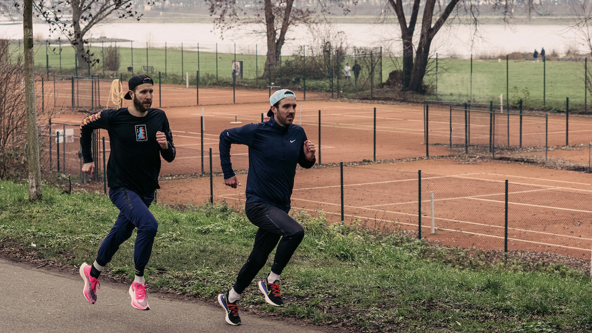 Zwei Läufer joggen an einem Tennisplatz vorbei