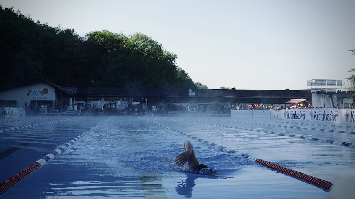 Ein Schwimmer schwimmt alleine auf einer Bahn im Freibad bei dampfenden Wasser