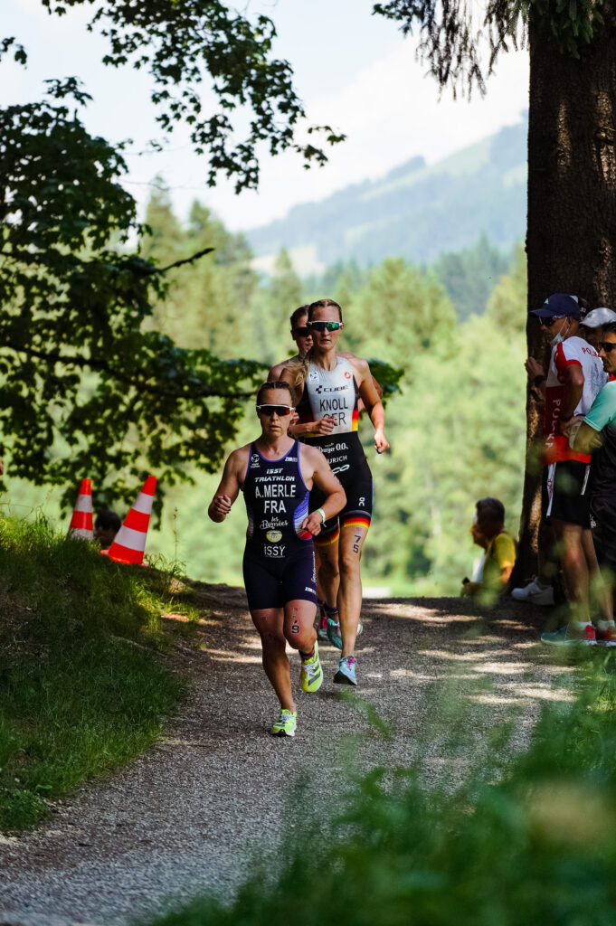 Anabel Knoll im Nationaltrikot läuft hinter einer Konkurrentin über einen Waldweg, am Rand Zuschauer