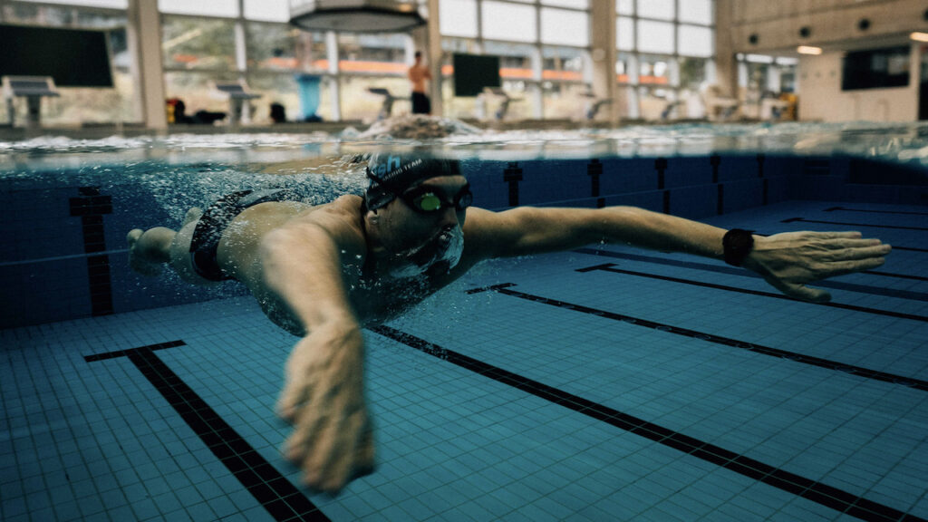 Unterwasseraufnahme eines Schwimmers mit Badekappe und Schwimmbrille beim Training im Hallenbad